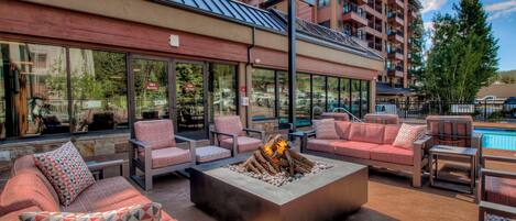 An outdoor seating area with sofas and chairs, a fire pit, and a view of a building with balconies.
