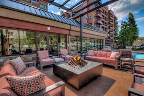An outdoor seating area with a fire pit, cushioned chairs, and a pool in the background. - On the River, Downtown Ski In/Out Location (Breckenridge)
