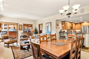 A spacious living room with a wooden dining table, comfortable seating, and a kitchen area with wooden cabinets and stainless steel appliances. - On the River, Downtown Ski In/Out Location (Breckenridge)