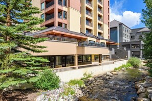 A multi-story hotel with balconies, a river, and surrounding greenery. - On the River, Downtown Ski In/Out Location (Breckenridge)