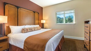 A hotel room with a bed, nightstands, a dresser, and a window with a mountain view. - Beautiful Riverside 2BR Condo in Estes Park over July 4th, 2026! (Estes Park)