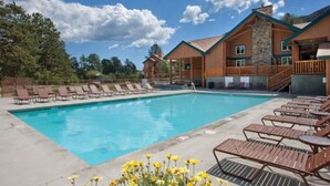 A pool area with lounge chairs and a building with a stone facade. - Beautiful Riverside 2BR Condo in Estes Park over July 4th, 2026! (Estes Park)