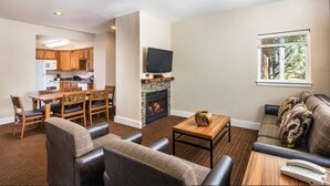 A living room with a fireplace, a television, a dining area with wooden furniture, and a sofa with patterned cushions. - Beautiful Riverside 2BR Condo in Estes Park over July 4th, 2026! (Estes Park)