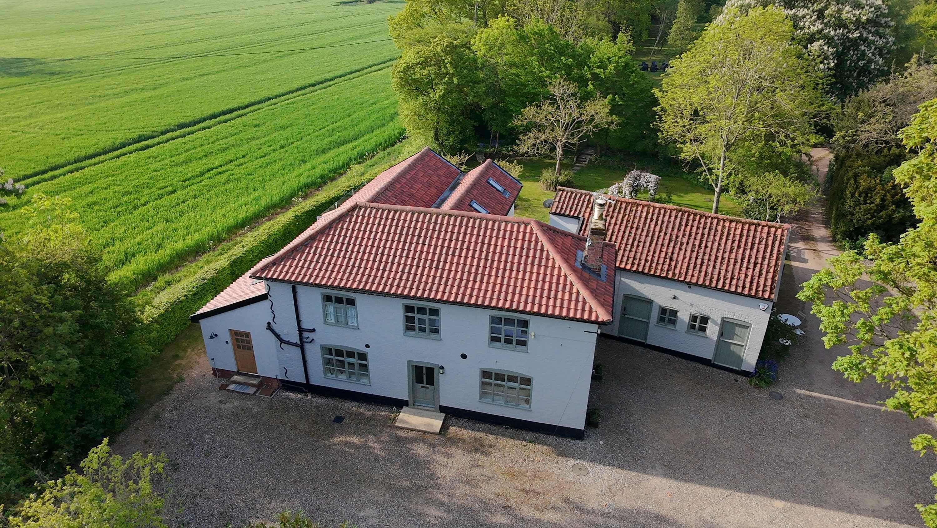 A two-story building with a red-tiled roof, surrounded by green fields and trees.