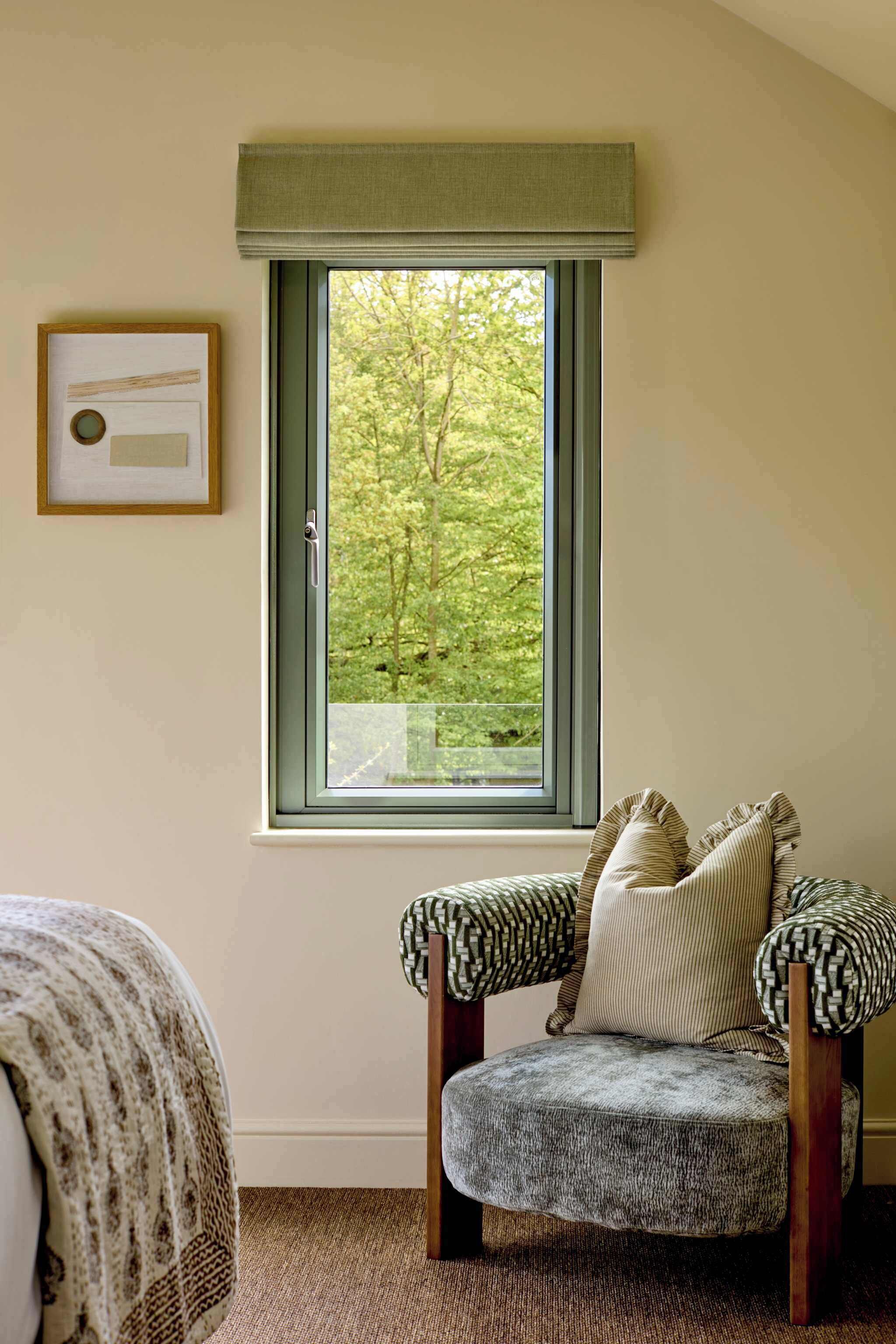 A room with a window, a framed picture, a chair, and a bed.