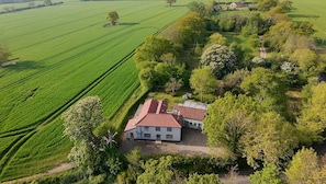 Una casa con techo de tejas rojas rodeada de campos verdes y árboles.