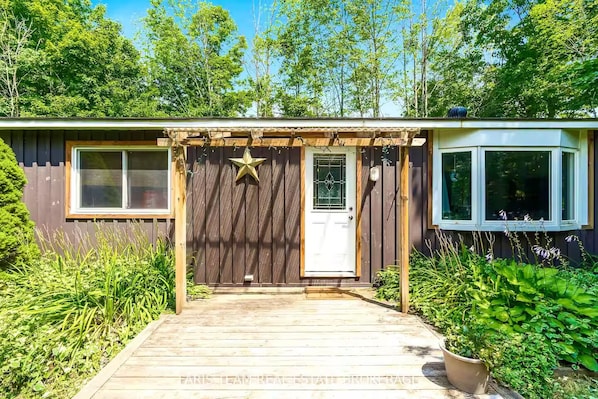 A wooden deck leading to a house with a star decoration, a white door, and a window on the right.