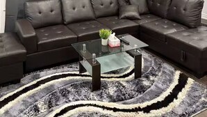 Una sala de estar moderna con un sofá modular, una mesa de centro de vidrio y un tapete estampado.