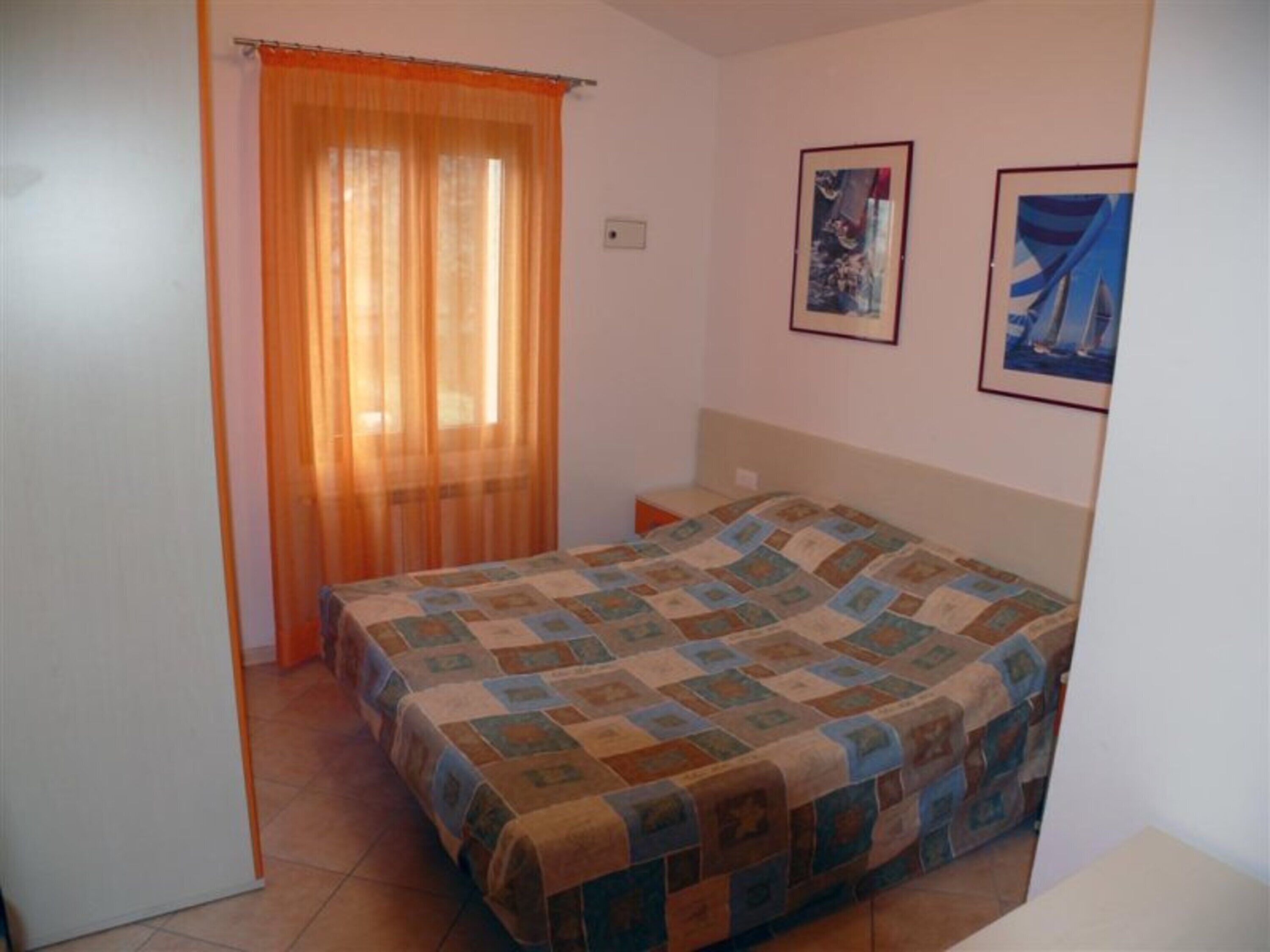 Une chambre à coucher avec un lit, une fenêtre avec des rideaux et deux tableaux encadrés accrochés au mur.
