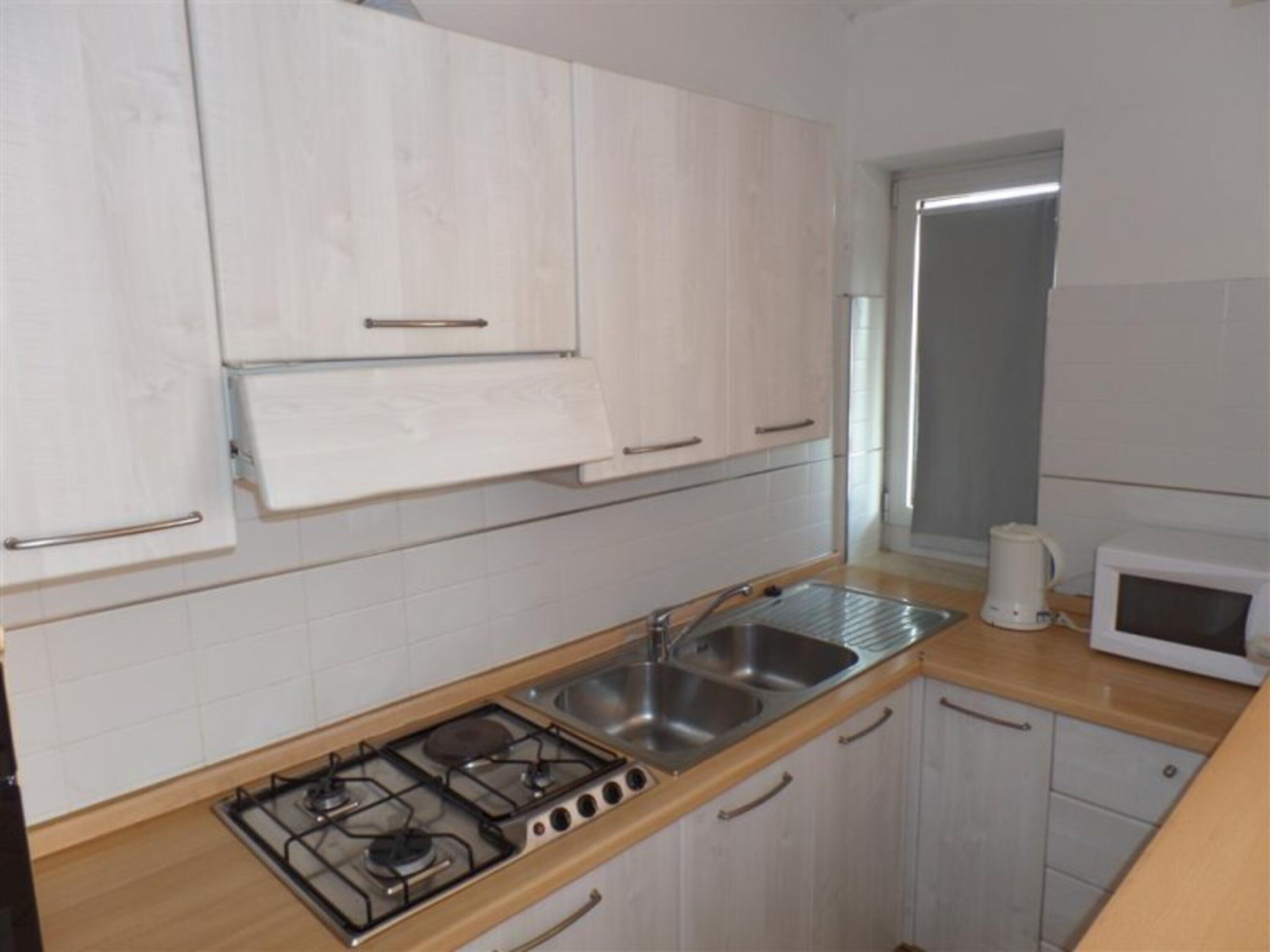 Una cucina con mobili bianchi, un piano cottura a gas, un lavello, un forno a microonde e una finestra.