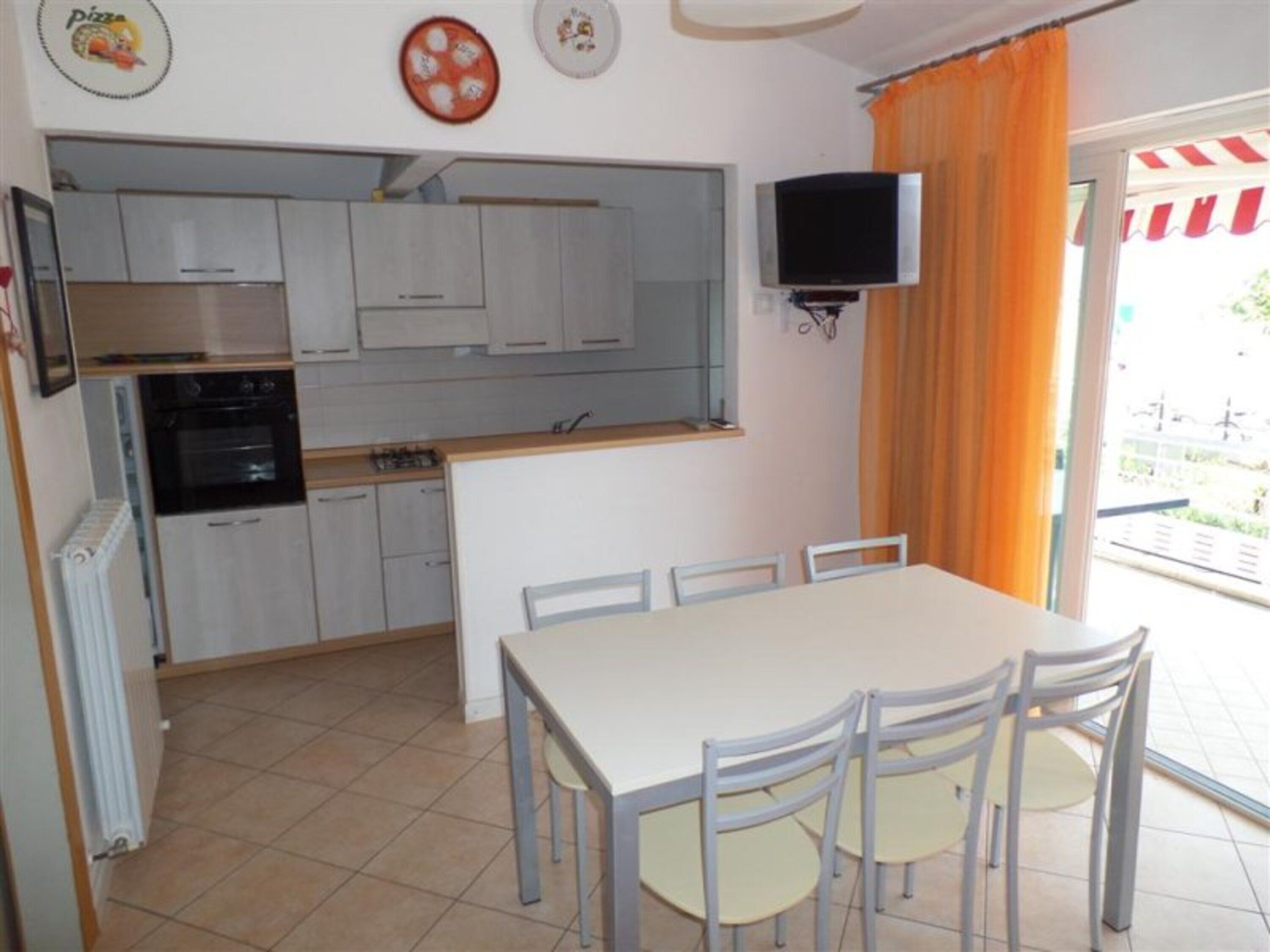Cucina con pensili bianchi, un fornello e un televisore fissato alla parete.
