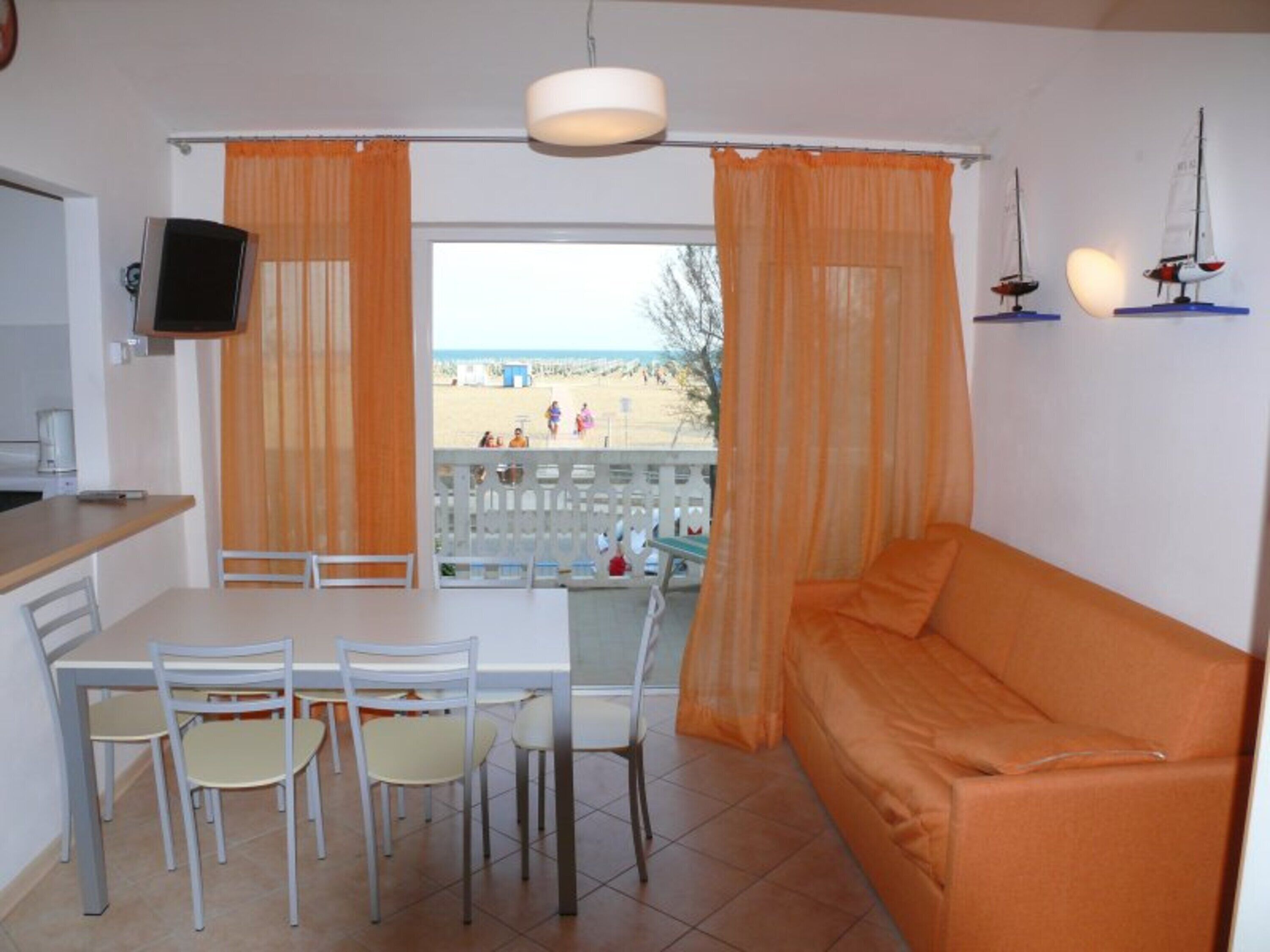 Ein Zimmer mit Esstisch, Stühlen, einer Couch, einem Fernseher und Blick auf den Strand.