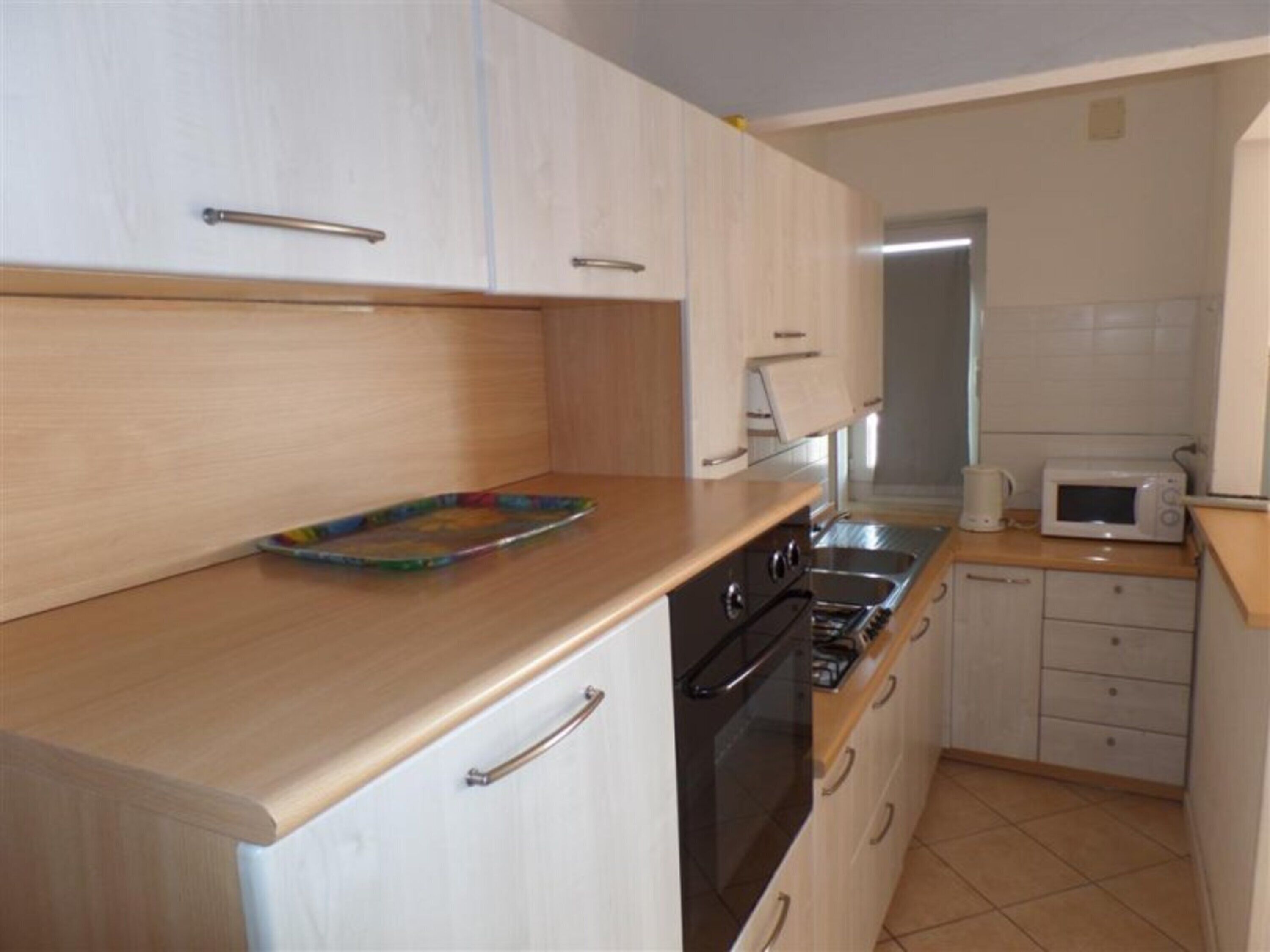 A compact kitchen with wooden cabinets, a microwave, a kettle, and a toaster.