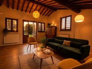 A cozy living room with a wooden ceiling, a green sofa, a yellow armchair, a wooden coffee table, and a potted plant.