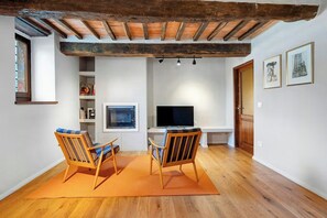Una sala de estar con televisión, dos sillas de madera, un sofá y techo de madera.