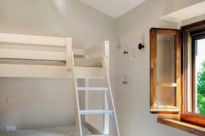 Una cama litera con escalera, una ventana con marco de madera y una lámpara fijada a la pared.