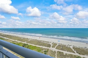 Ein Strand mit blauem Himmel, einem Steg und einem Sandweg, der zum Wasser führt.