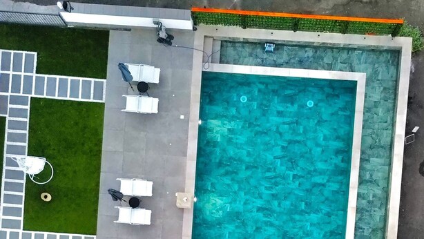 Vue aérienne d’une piscine entourée d’espaces de détente, d’une petite terrasse et d’un chemin pavé.