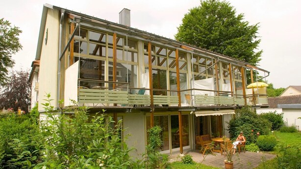 Une maison à deux étages avec un balcon, un jardin et un petit espace patio.