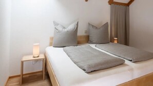 Une chambre à coucher comprenant un lit, deux tables de chevet, une commode, une chaise en bois et un rideau.