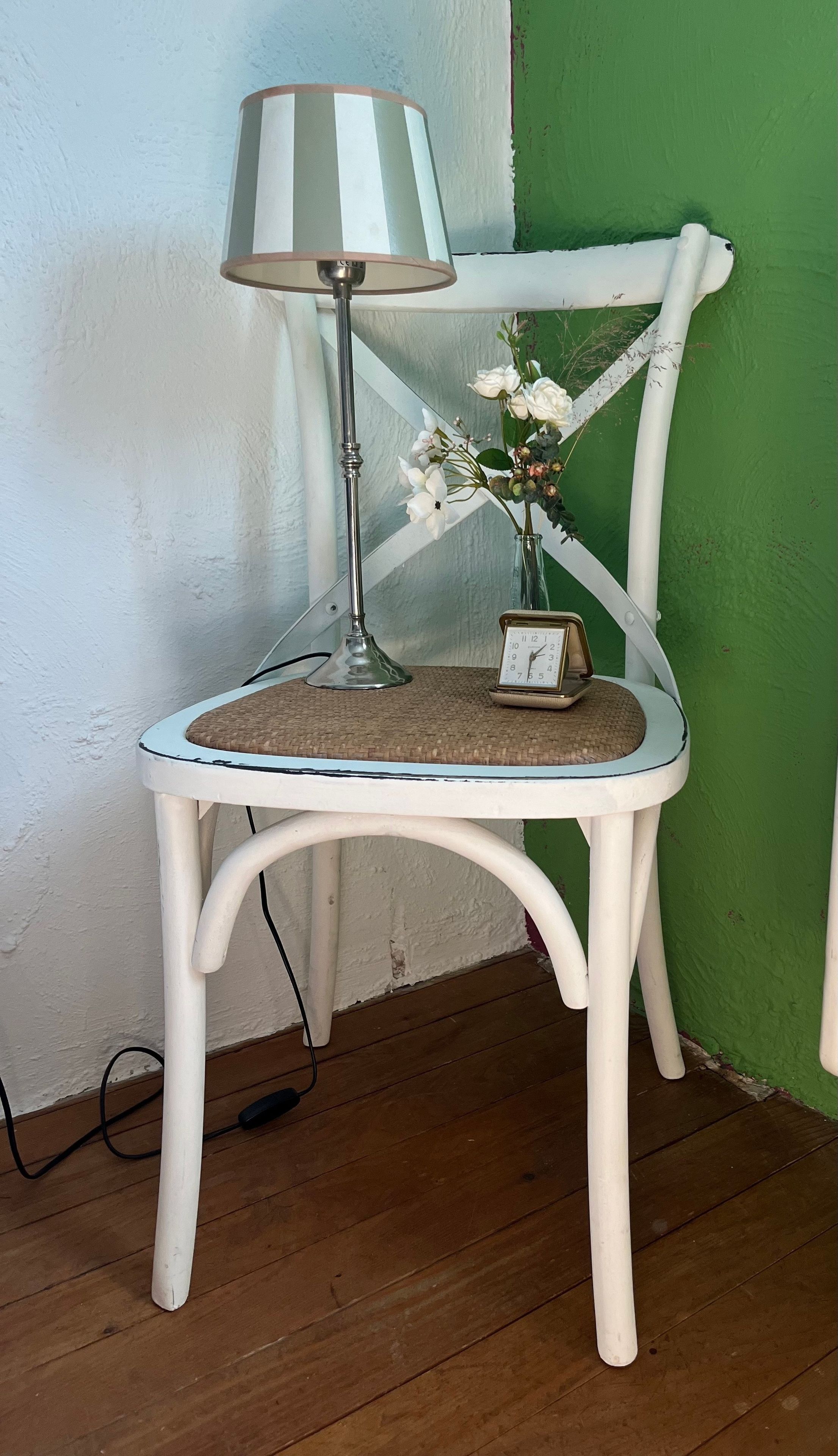 A white chair with a woven seat cushion, a table lamp, and a small clock on the chair.