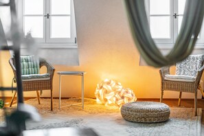 Et værelse med fletstole, et lille bord, en vævet skammel og en dekorativ lampe.