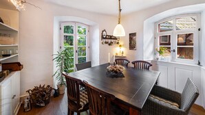 Un espace repas comprenant une table en bois, des chaises, un luminaire suspendu et une fenêtre donnant sur un paysage verdoyant.