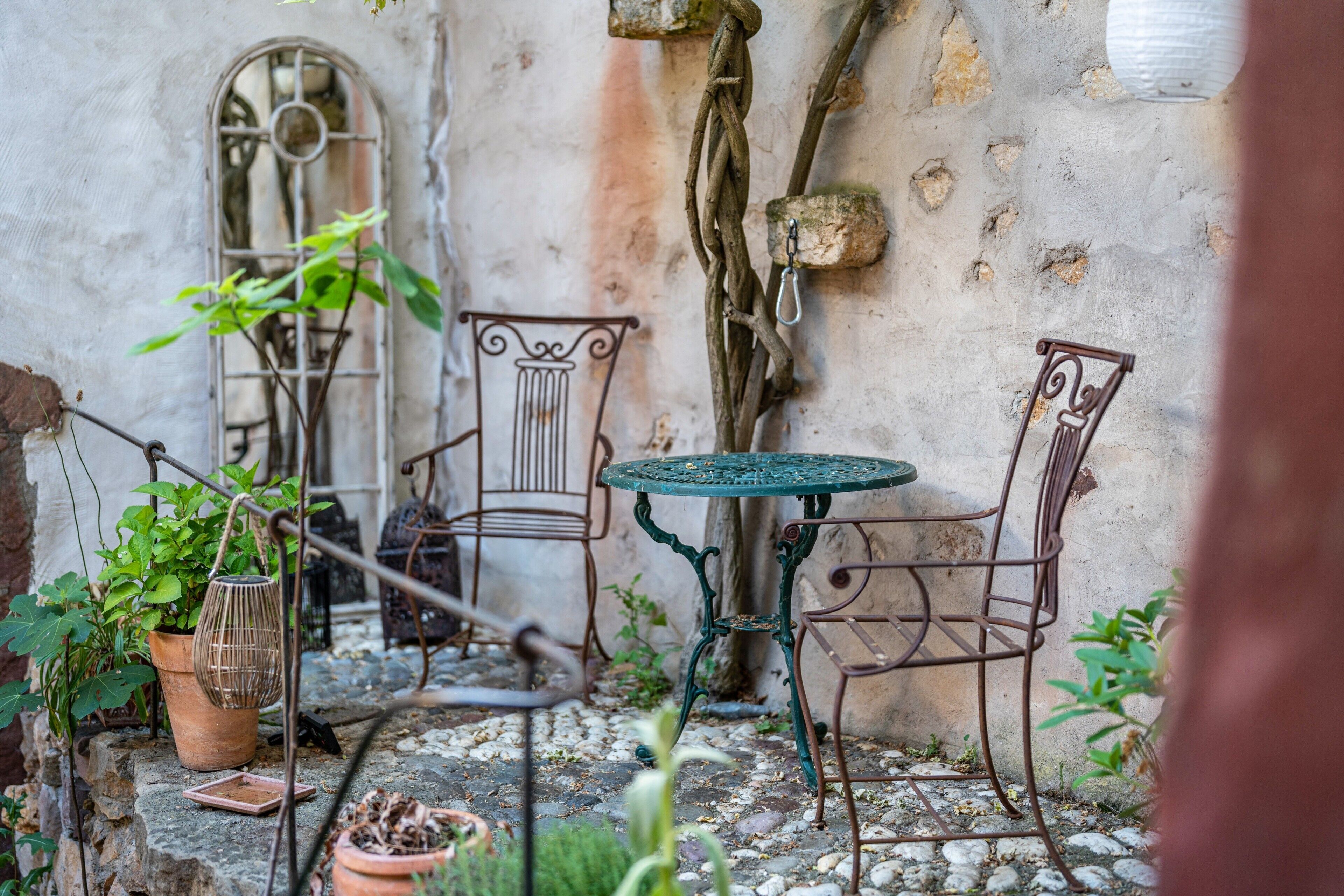 Un espace extérieur aménagé avec des chaises en métal et une table, entouré de plantes en pot et doté d’un sol en pierre.