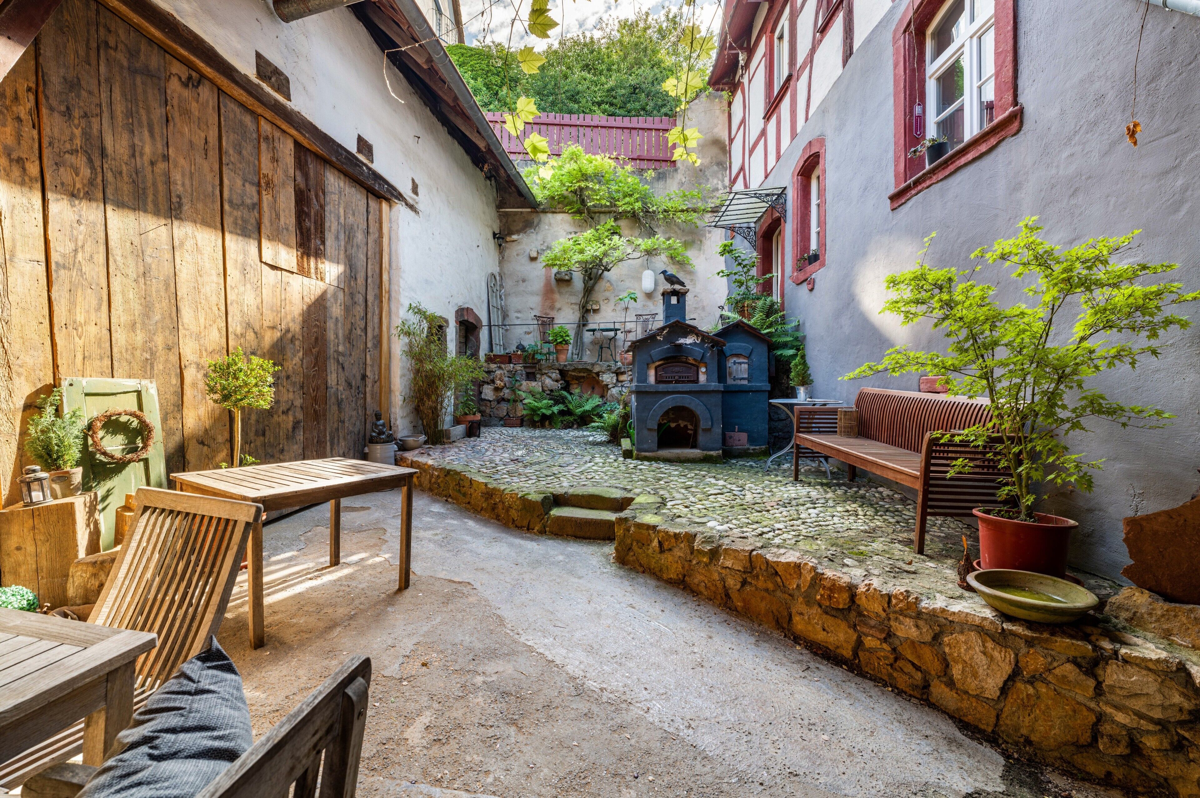 A courtyard with stone flooring, wooden furniture, and potted plants.