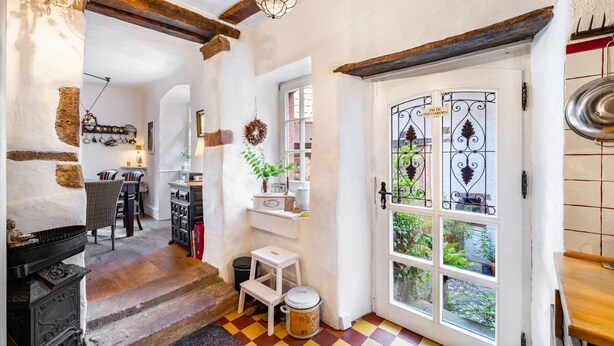 Un intérieur rustique avec des poutres apparentes, une cheminée, un coin repas et une vue à travers une porte vitrée.