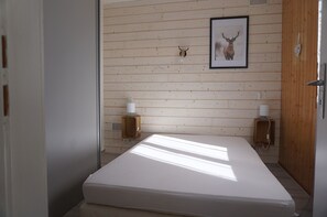Ein Zimmer mit einem Bett, Holzwänden, einem Bild von einem Hirsch und zwei Wandlautsprechern.