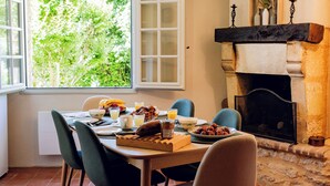 Un comedor con una mesa lista para el desayuno, una chimenea y vistas a la vegetación exterior.
