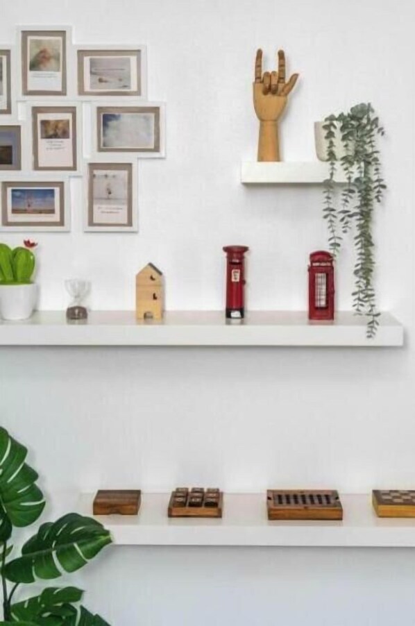 Dos repisas blancas con varios objetos decorativos, incluyendo cuadros enmarcados, una mano de madera, una planta, pequeñas figuras y un teléfono rojo.