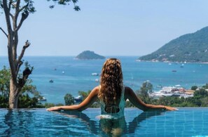 A person in a swimming pool with a view of the sea and distant land.