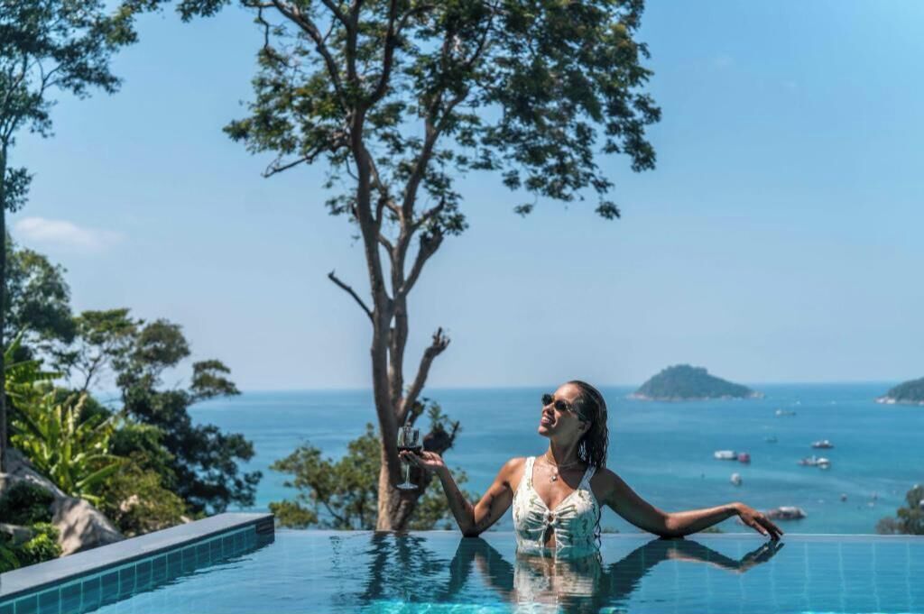 Une personne dans une piscine, avec une vue dégagée sur l’océan et un arbre.