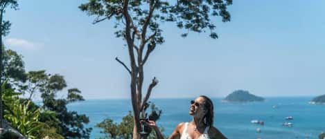 A person in a swimming pool with a clear view of the ocean and a tree.