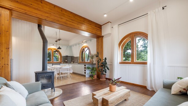 A cozy living room with a sofa, a wooden coffee table, and a fireplace. There is a kitchen in the background with a dining area.