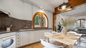 A modern kitchen with white cabinetry, a large window, and a dining area with a wooden table and chairs.