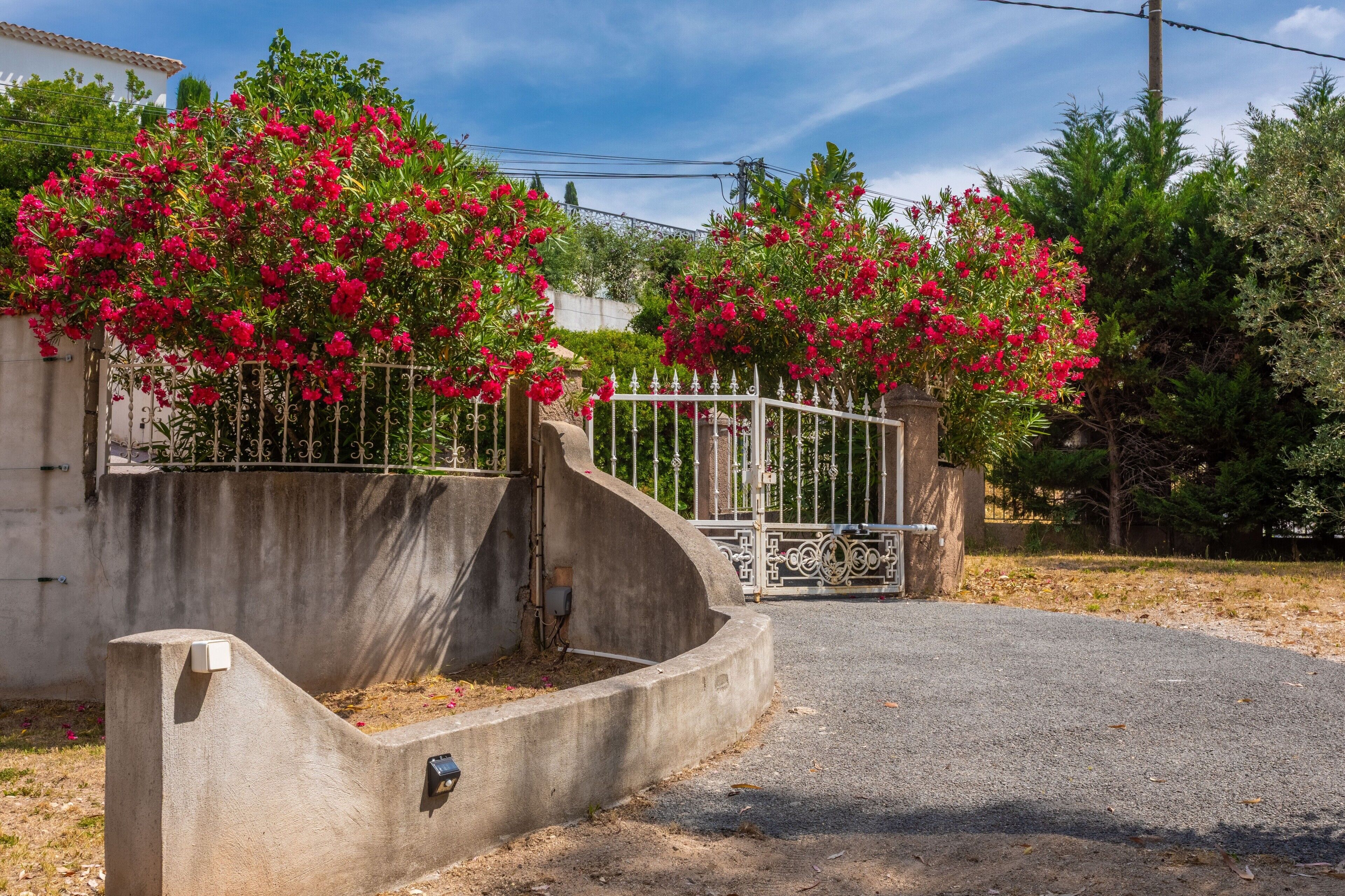Une entrée fermée par un portail, avec un parterre en béton, un portail en métal et un ciel dégagé.
