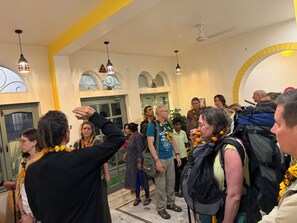 A group of people in a room with arched windows, a yellow accent wall, and pendant lighting.