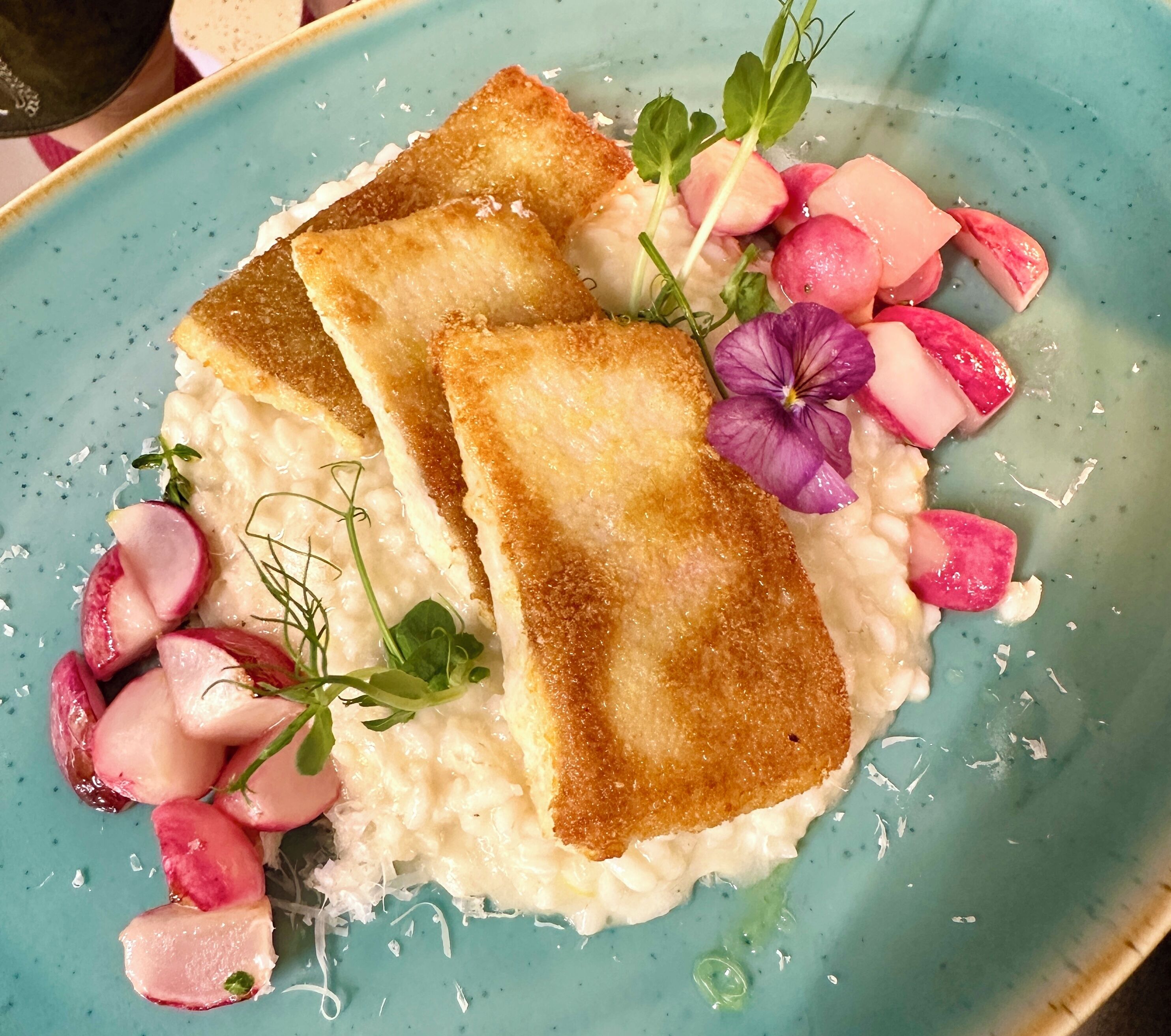 Ein Teller mit pochierten Eiern, geröstetem Brot, Radieschen und einer violetten Blüten-Garnitur.