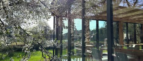 Un edificio moderno con grandes ventanales, techo de madera y vistas a un jardín con árboles florecientes.