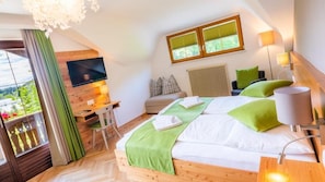 A bedroom with a bed, a TV, a desk, a chair, a window, and a balcony.