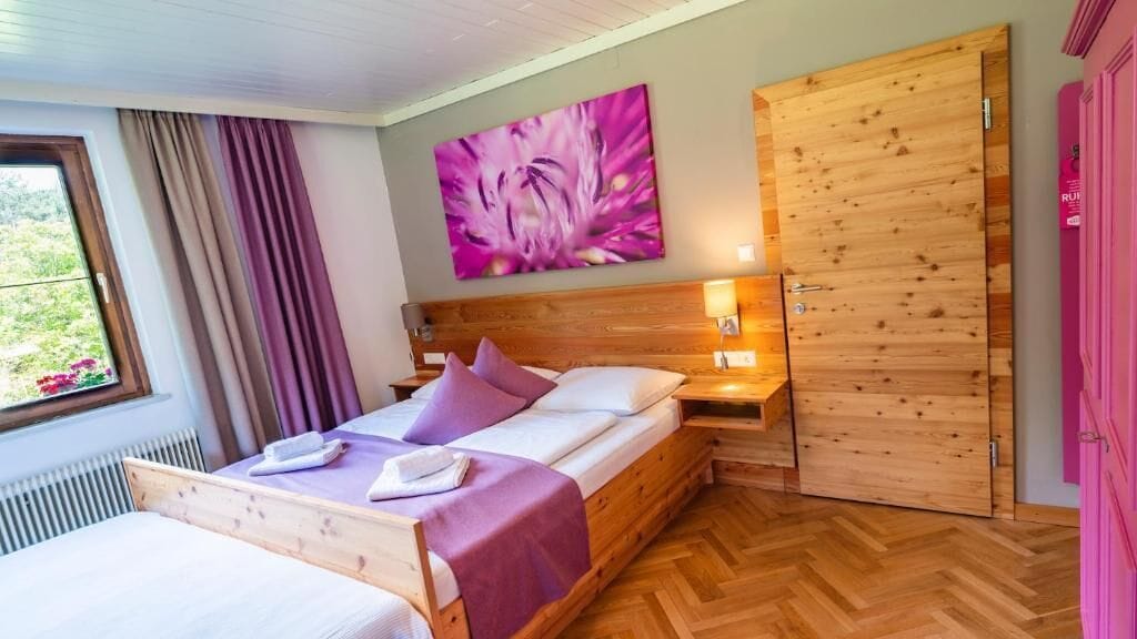 A bedroom with a bed, wooden headboard, a wall-mounted artwork, a wooden wardrobe, and a window with curtains.