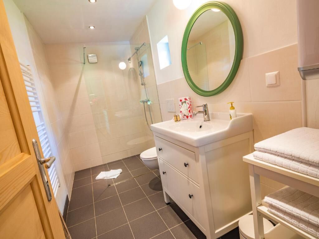 A bathroom with a shower, toilet, white vanity with a mirror, and a towel rack.