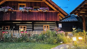 A wooden log cabin with a balcony, a wooden fence, and a garden with flowers. - Genussgasthof Feidig (Velden am Worther See)