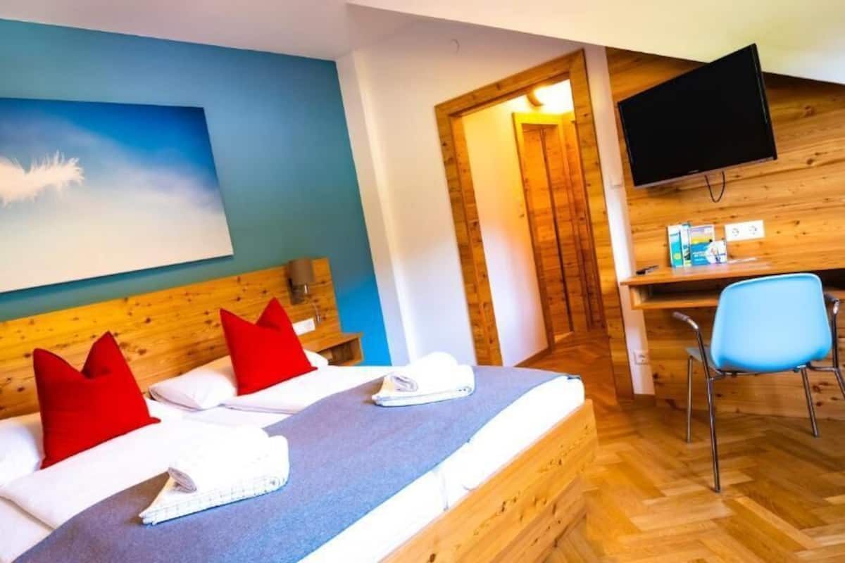 A hotel room with a bed, a desk, a chair, a television, and a painting on the wall.