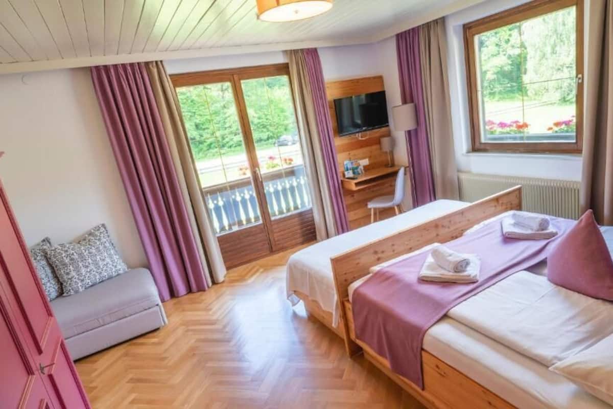 A bedroom with two beds, a desk, a TV, and a balcony.