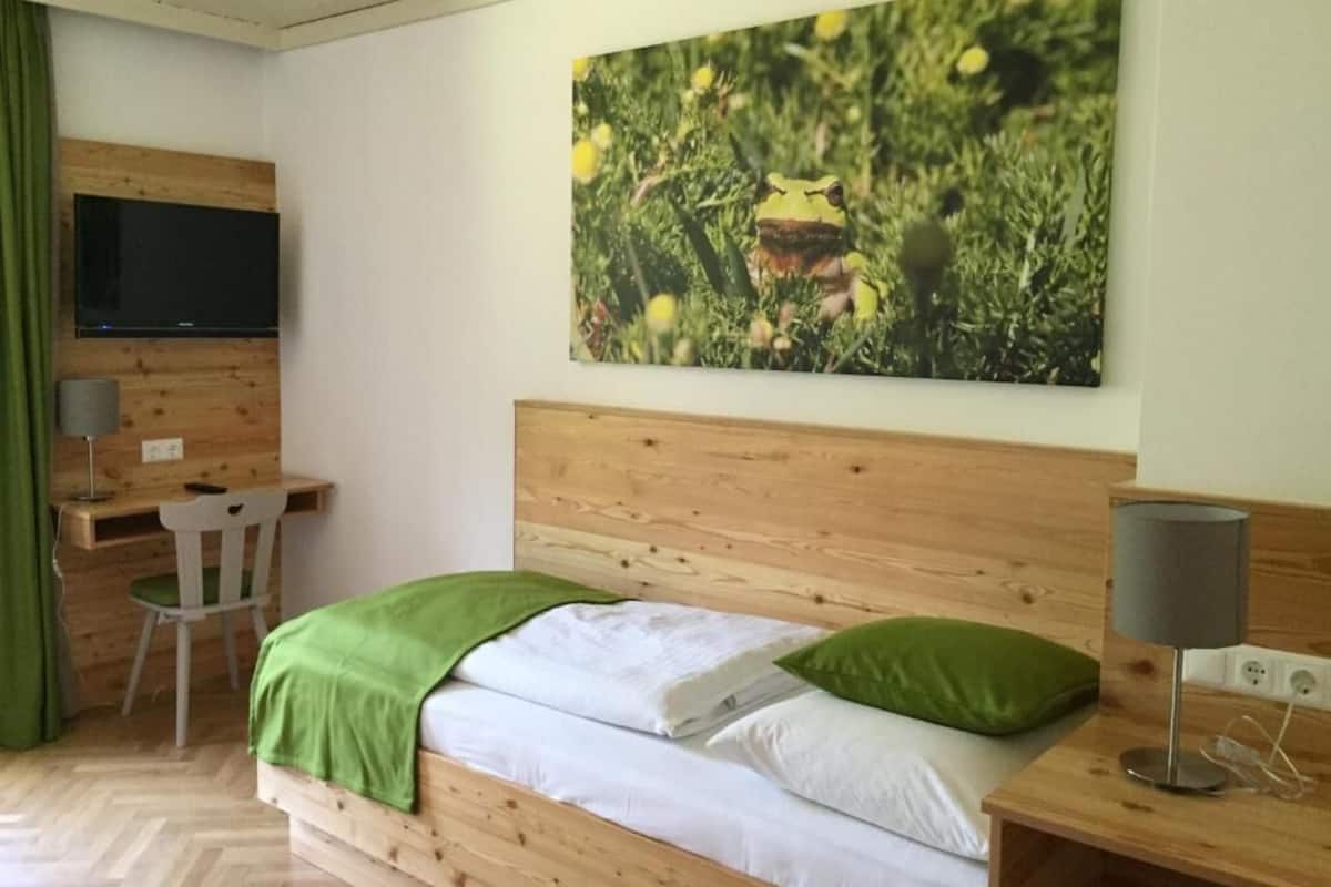 A bedroom with a wooden bed, a desk, a chair, a TV, and a wall-mounted lamp.