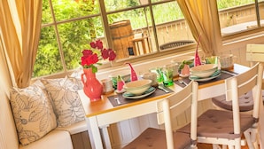 A dining area with a table set for four, a vase with flowers, and a view of greenery through large windows. - Genussgasthof Feidig (Velden am Worther See)